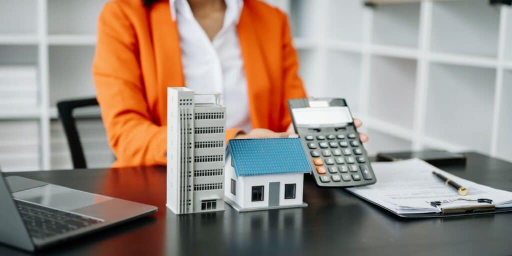 A real estate agent's desk with scale models of a commercial building and a house, alongside a calculator